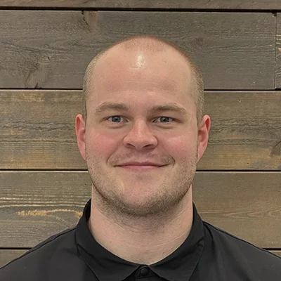 Jacob McDonald smiling in front of a stone wall.